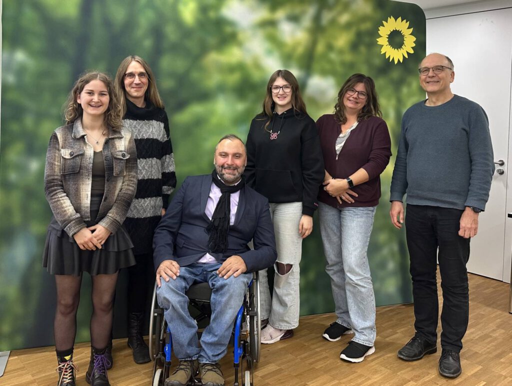 Nach der Veranstaltung positionierten sich mehrere Personen vor dem Hintergrund der Grünen Partei. Oben rechts ist die typische Sonnenblume zu sehen. Von links nach rechts: Vanessa Seidel, Patrick Alberti, Mohamed Zakzak, Sophia Schad, Simone Rehberger und Martin Wilmes.