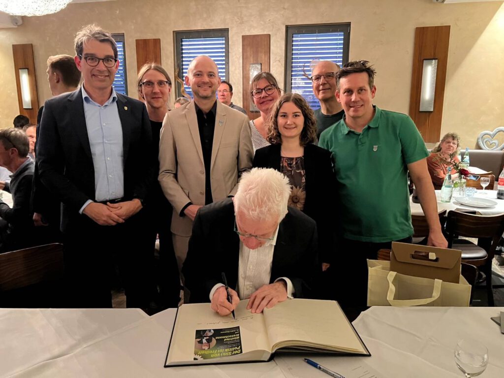Ministerpräsident Kretschmann trägt sich in das Goldene Buch der Gemeinde ein. Im Hintergrund Dr. Andre Baumann, Bürgermeister Pascal Seidel und Mitglieder des Grünen OV